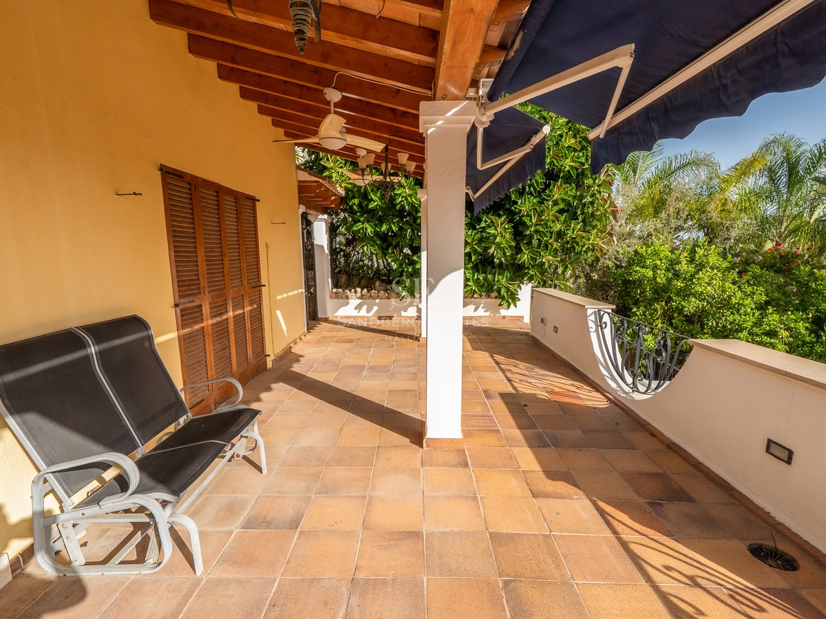 Sonnige Terrasse mit Terrakottafliesen, Holzbalken an der Decke, Deckenventilator und blauer Markise.