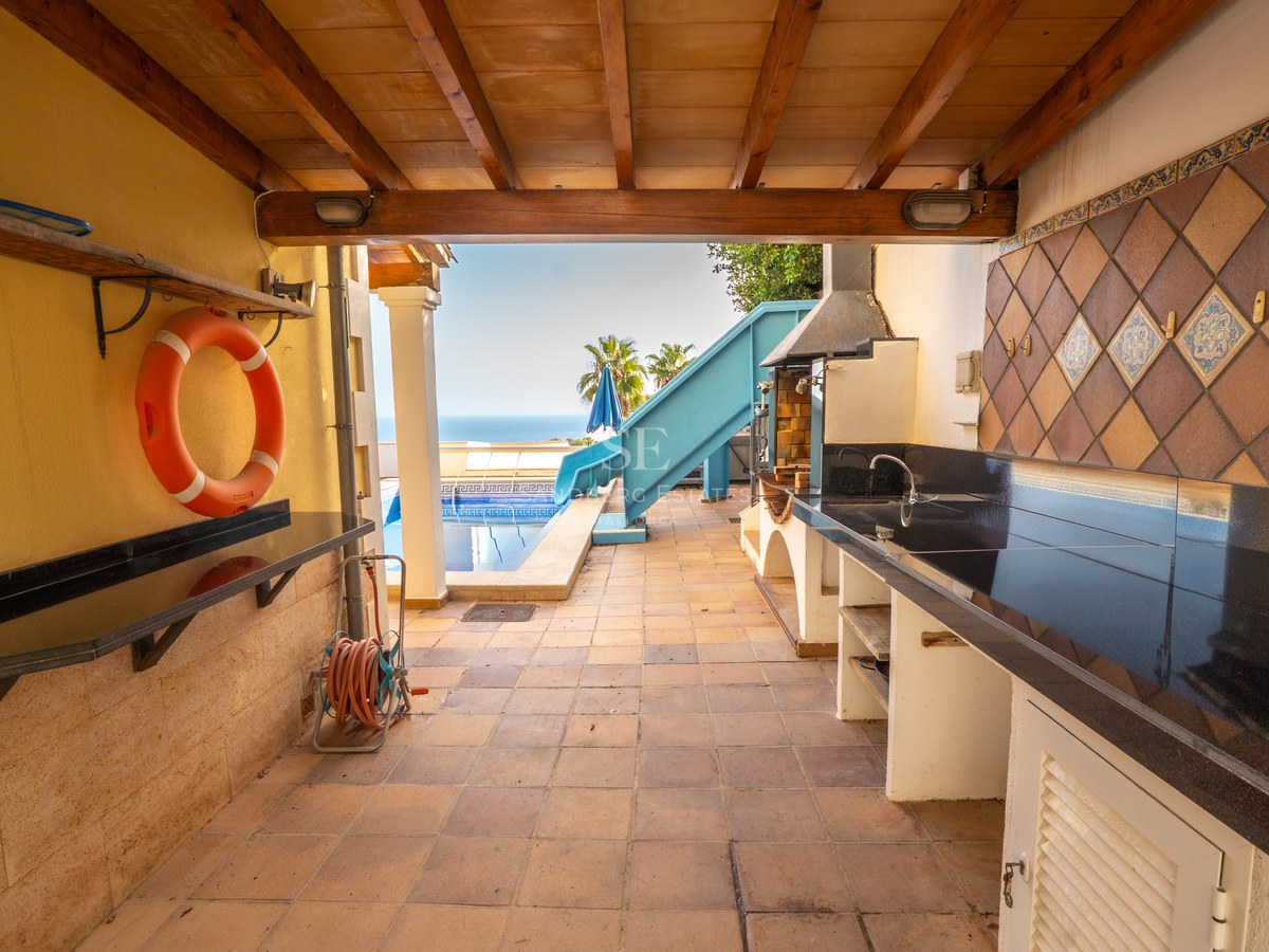 Außenküche auf einer überdachten Terrasse mit Grill, schwarzen Arbeitsplatten und Blick auf den Pool und das Meer.