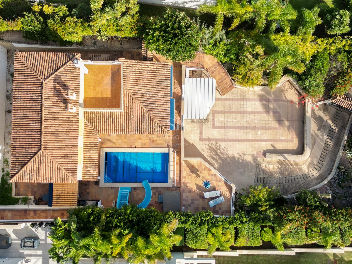 Vogelperspektive einer Villa mit Terrakottadach, blauem Pool mit Rutsche und üppigen grünen Gärten.