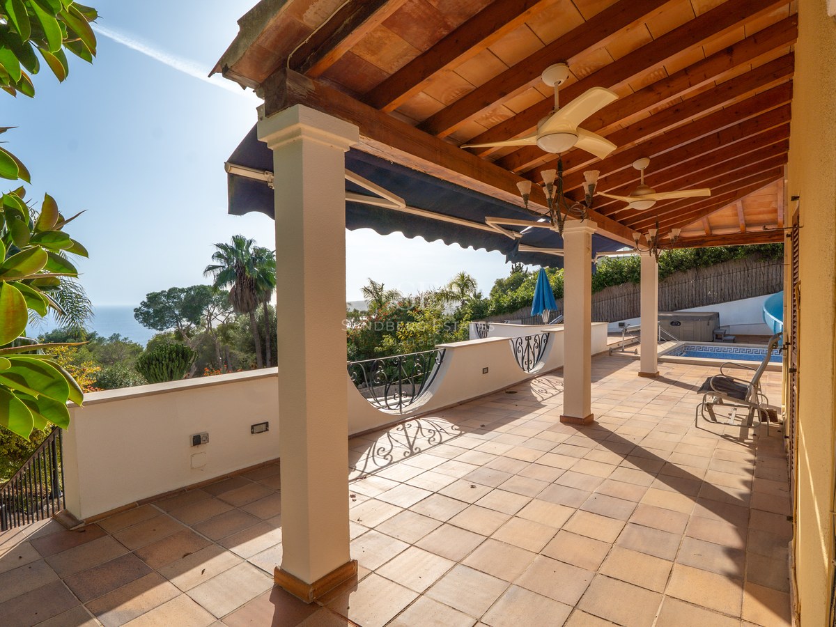 Große überdachte Terrasse mit weißen Säulen, Terrakottaboden und Panoramablick auf das Meer.