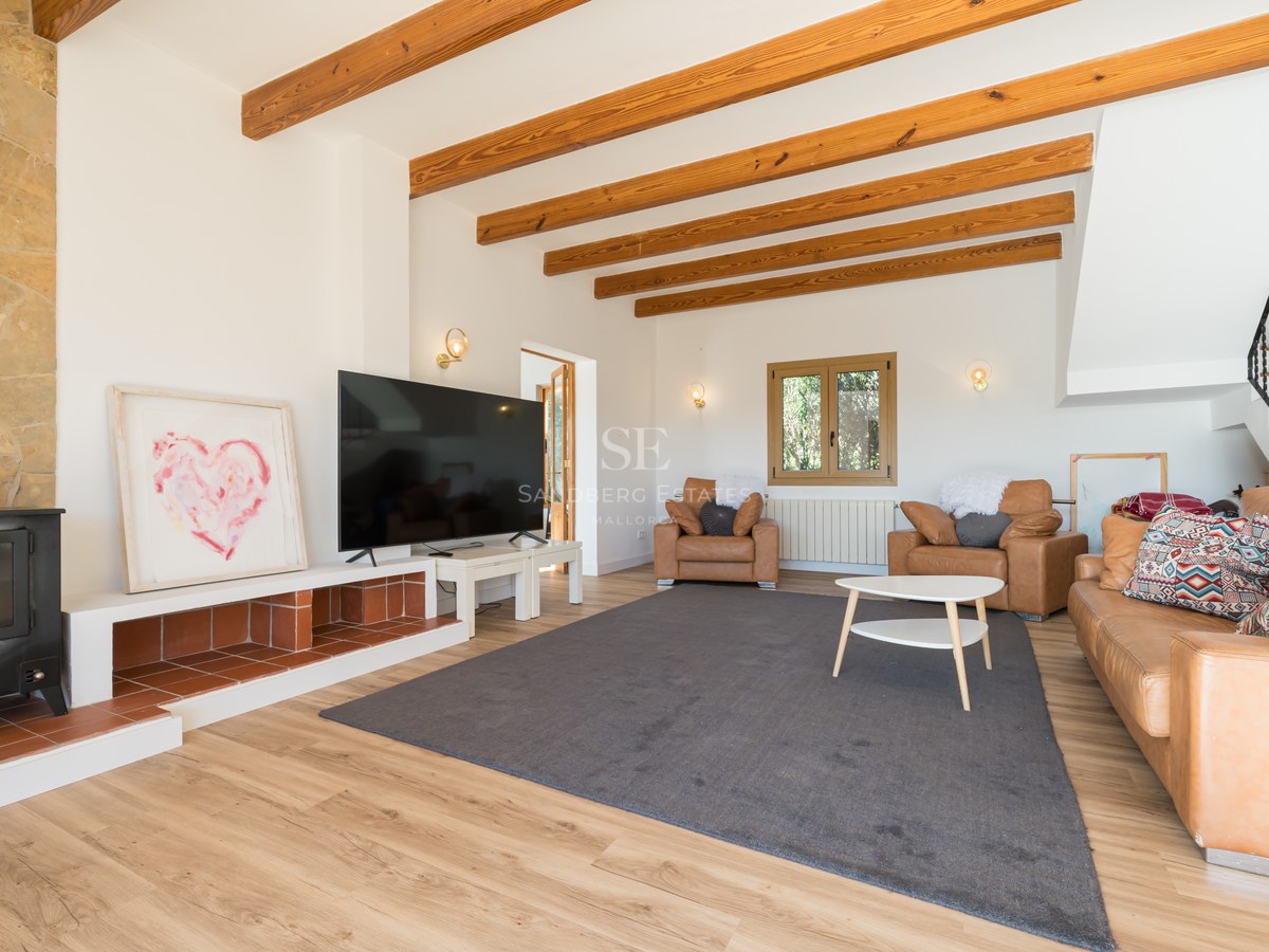 Acogedor salón con vigas de madera a la vista, estufa de leña negra, sofás de cuero y una televisión grande.