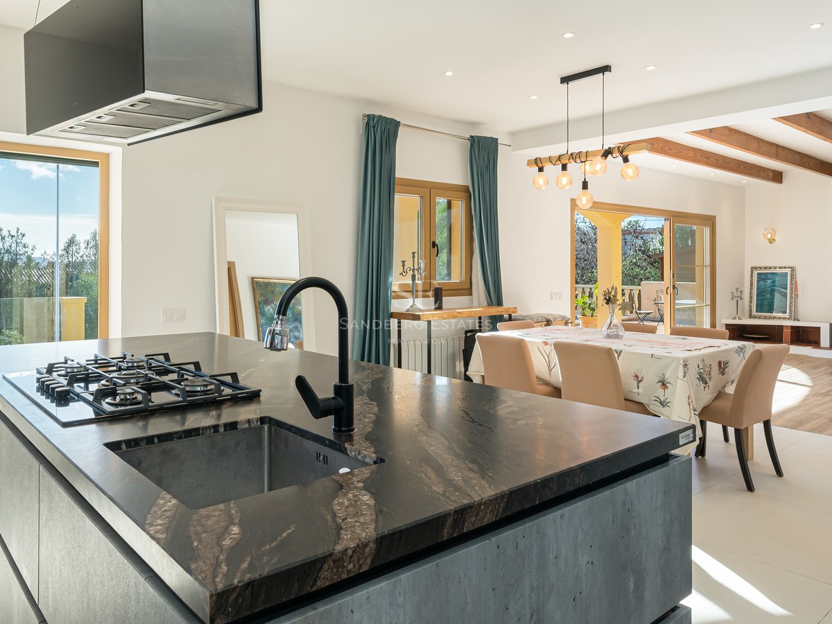 Isla de cocina moderna con encimera de piedra oscura que da a un comedor y sala de estar con chimenea.