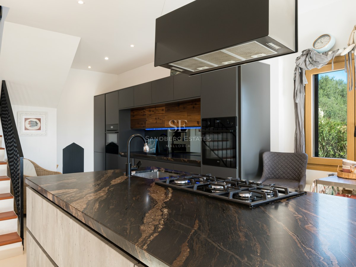 Cocina moderna con isla de mármol negro, estufa de gas y ventana con vistas a las montañas.