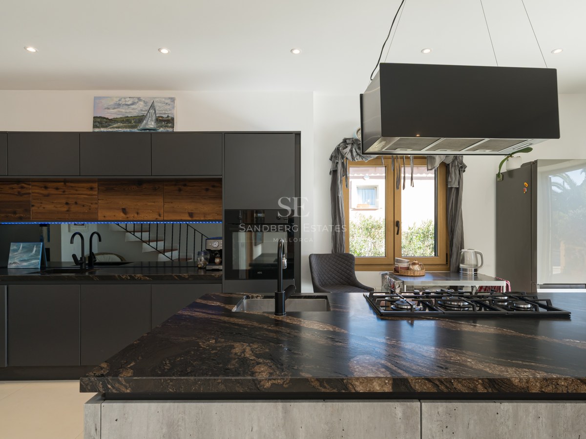 Cocina moderna con isla de mármol oscuro, armarios negros mate y detalles en madera.