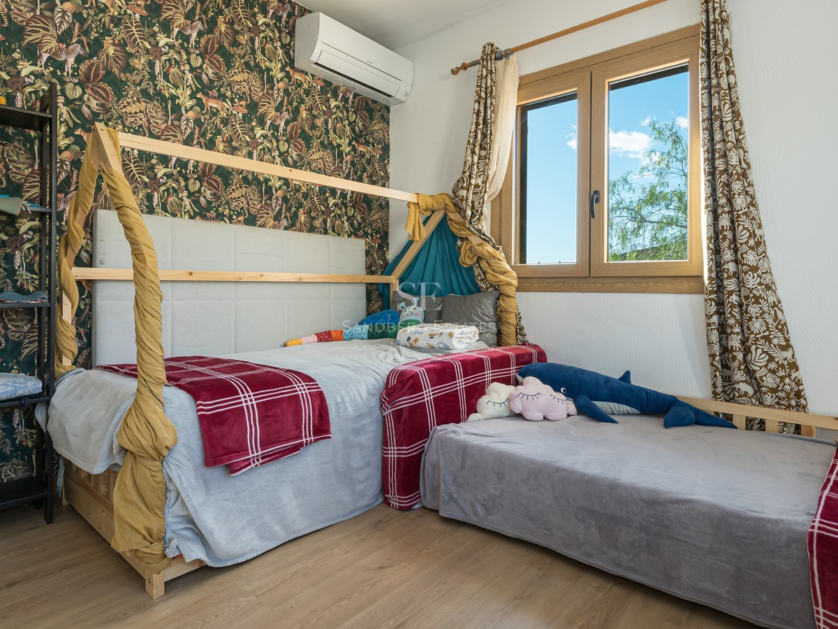 Dormitorio infantil con cama de madera en forma de casita, papel de jungla y luz natural.