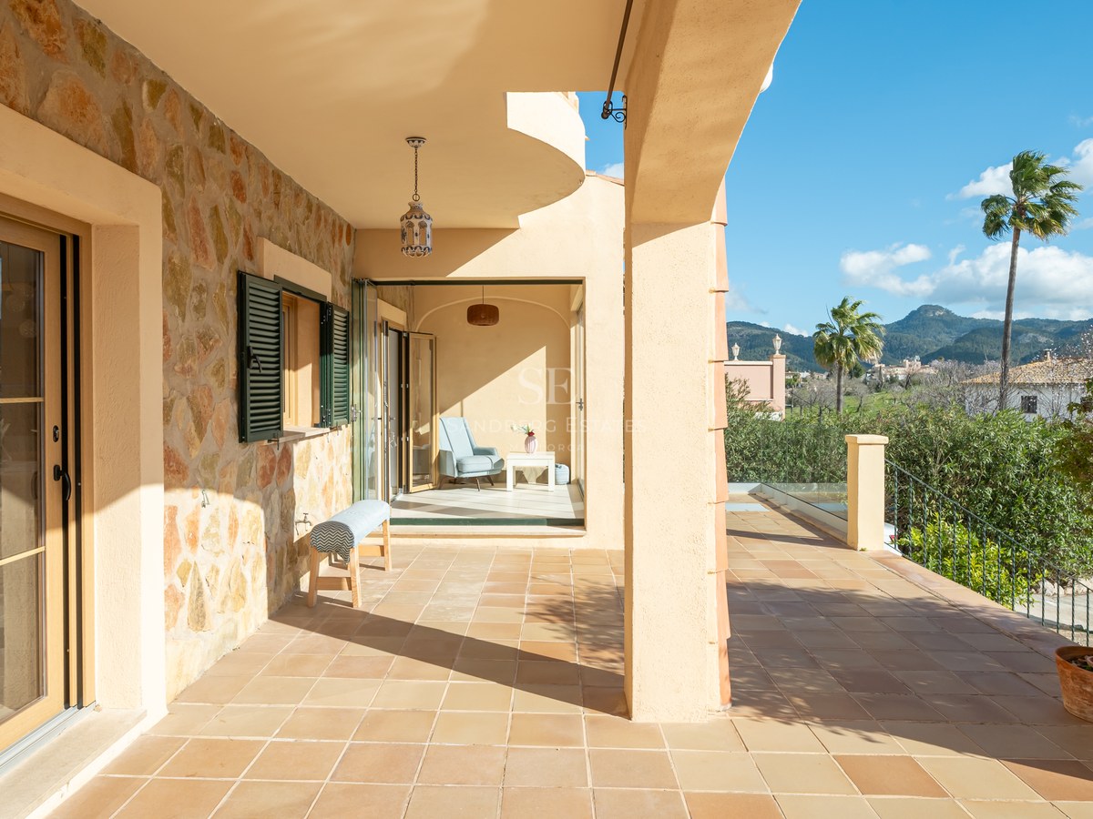 Terraza cubierta con suelos de terracota y pared de piedra natural con vistas a colinas verdes y montañas.