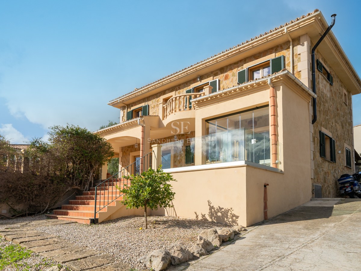 Villa mediterránea de dos plantas con muros de piedra natural, tejado de terracota y terraza acristalada.