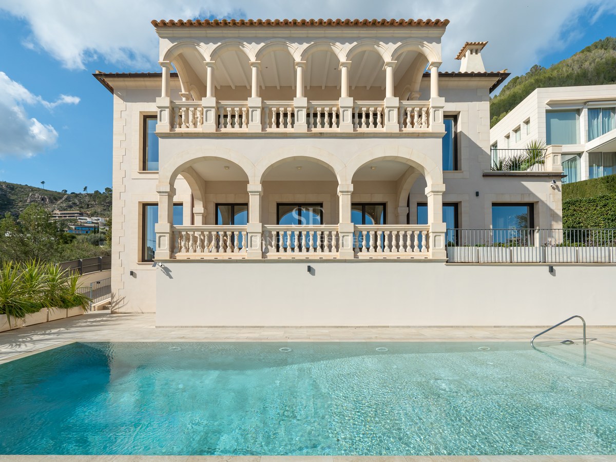 Vista exterior de una villa de piedra color arena con arcos clásicos y una gran piscina turquesa en primer plano.