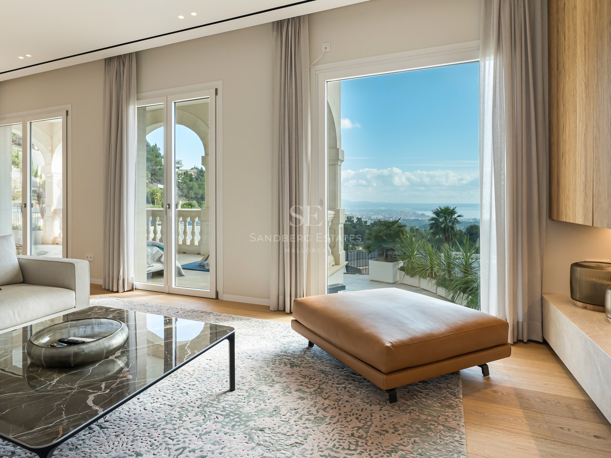 Salón moderno con mesa de mármol, otomana de cuero y ventanales con vistas al mar Mediterráneo.