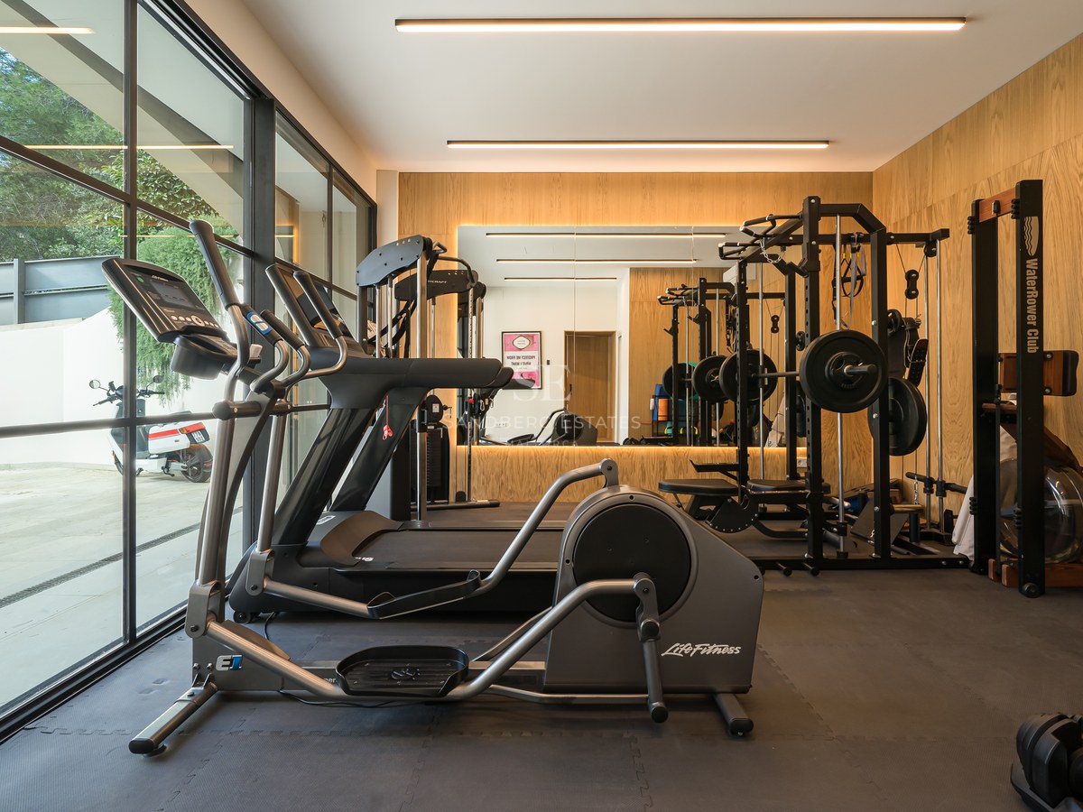 Gimnasio moderno con equipamiento de alta gama, paredes paneladas en roble y grandes ventanales.