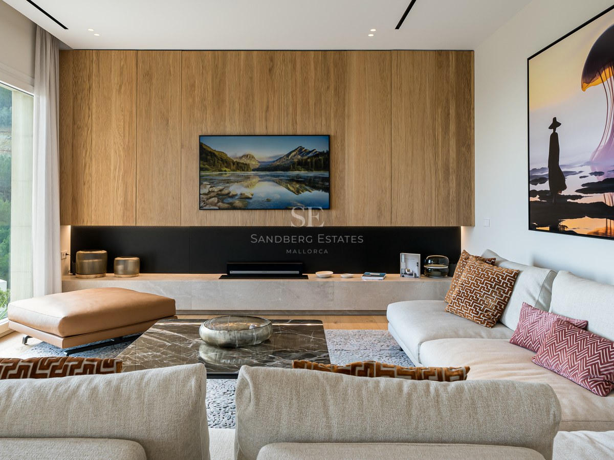 Salón moderno con pared de listones de madera, televisión integrada y ventanales con vistas a la naturaleza.