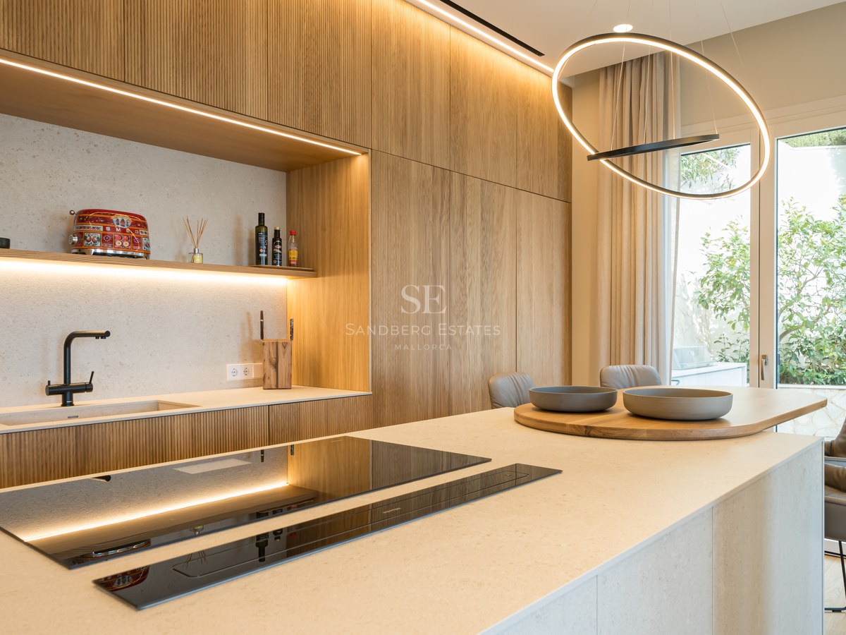 Cocina moderna con armarios de roble fresado, isla de piedra, placa de inducción y puerta de cristal al jardín.