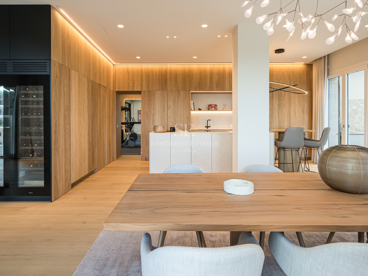Comedor moderno con mesa de roble, vinoteca de lujo e iluminación LED integrada en una vivienda de concepto abierto.