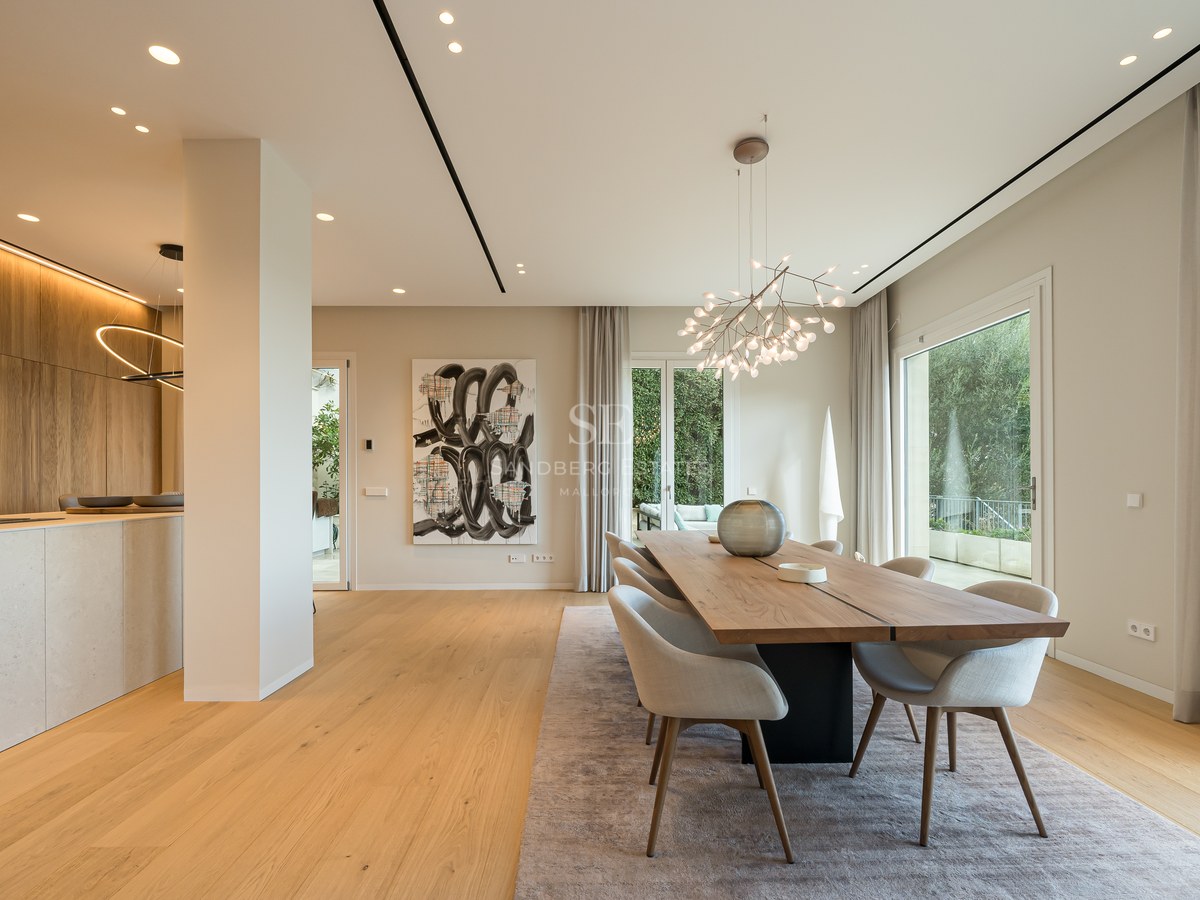 Comedor moderno con mesa de madera, sillas grises, lámpara de diseño y ventanales hacia la terraza.