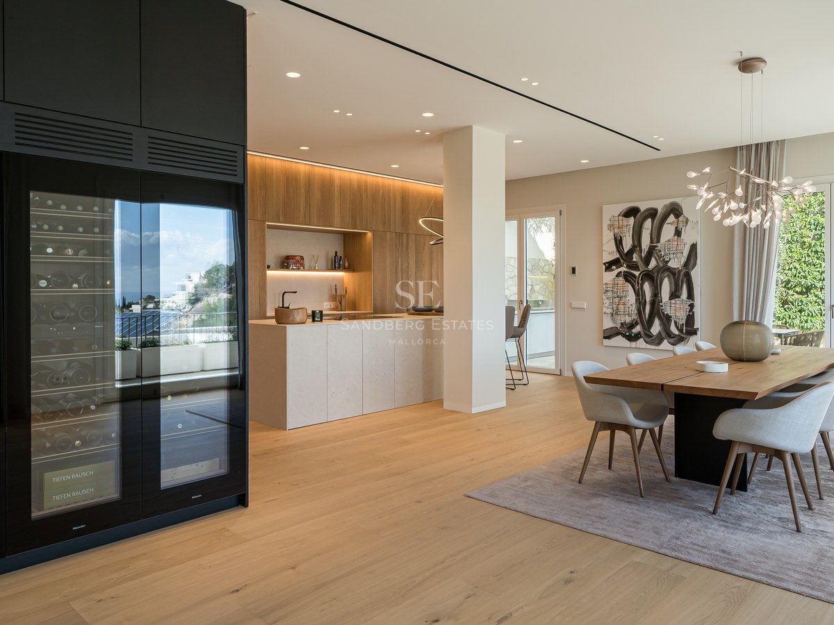 Comedor moderno de planta abierta con mesa de madera maciza, sillas tapizadas y vinoteca profesional empotrada.
