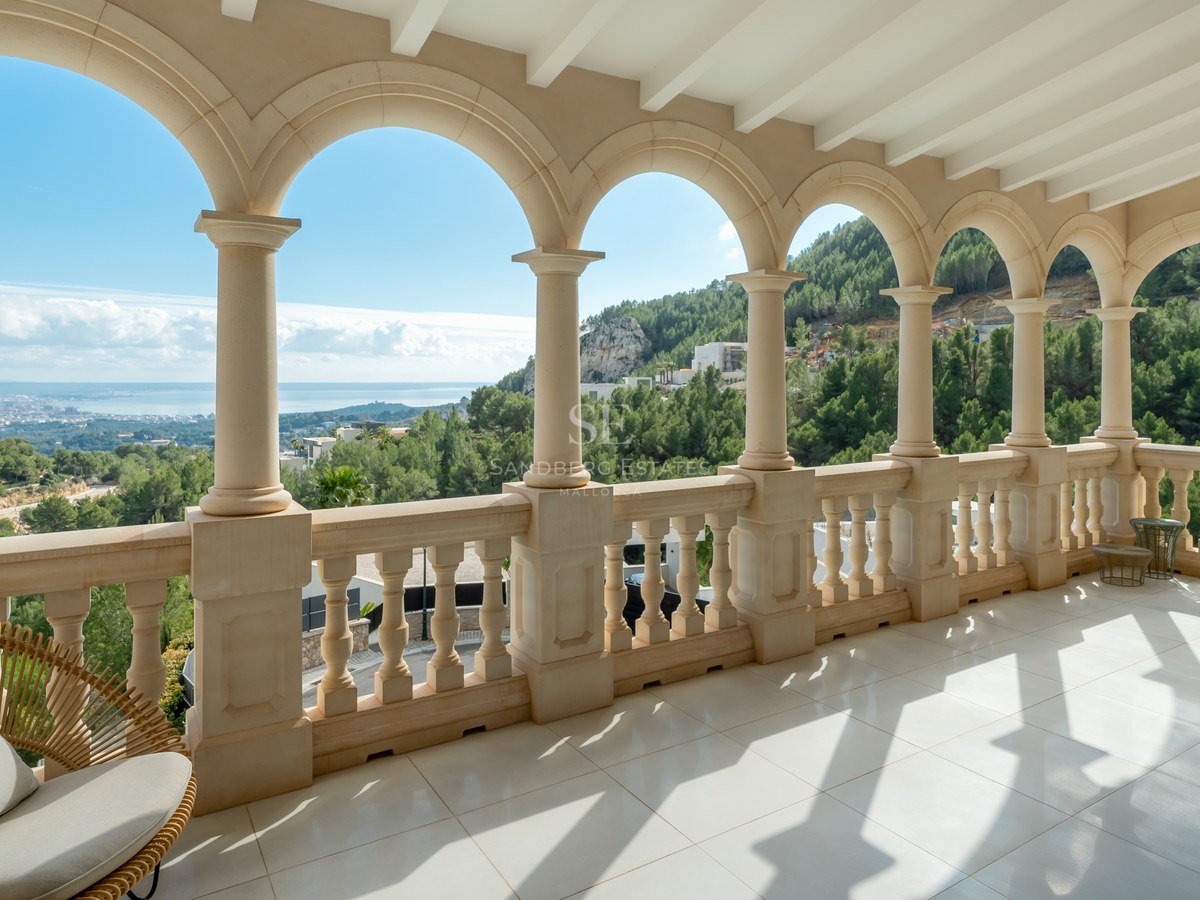 Terraza de piedra con arcos clásicos y vistas a colinas verdes, el mar y la silueta de la ciudad.