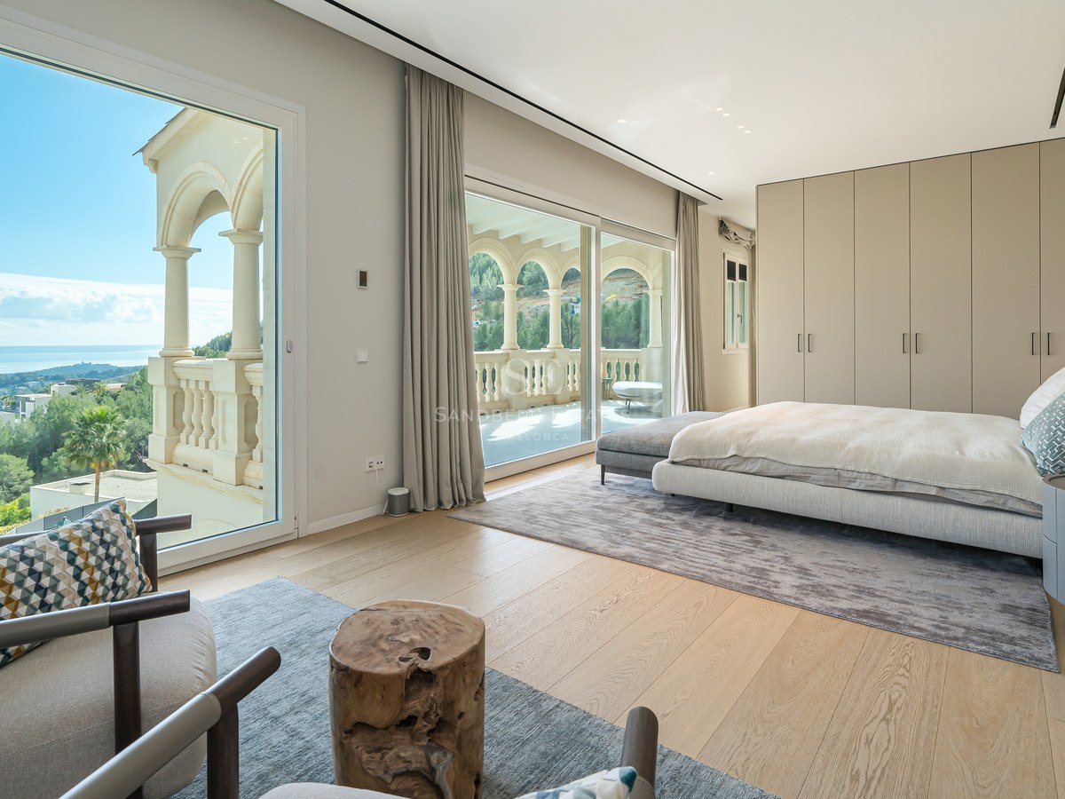 Dormitorio principal moderno con ventanales de suelo a techo, suelos de roble claro y balcón privado con vistas a la costa.