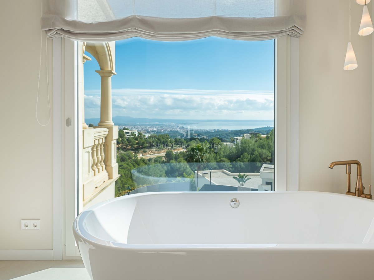 Bañera exenta blanca frente a un gran ventanal con vistas panorámicas a la costa y la ciudad.