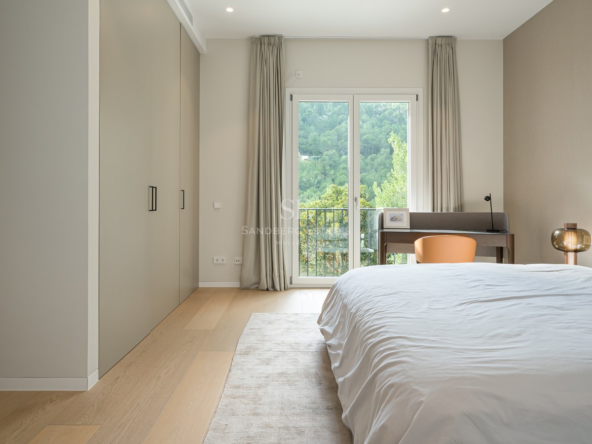 Dormitorio moderno con armarios de suelo a techo, suelos de madera clara y puertas francesas con vistas al bosque.