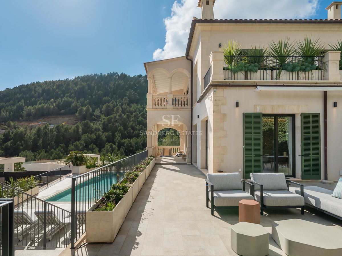 Terraza de lujo con mobiliario moderno, vistas a una piscina y montañas boscosas bajo un cielo despejado.