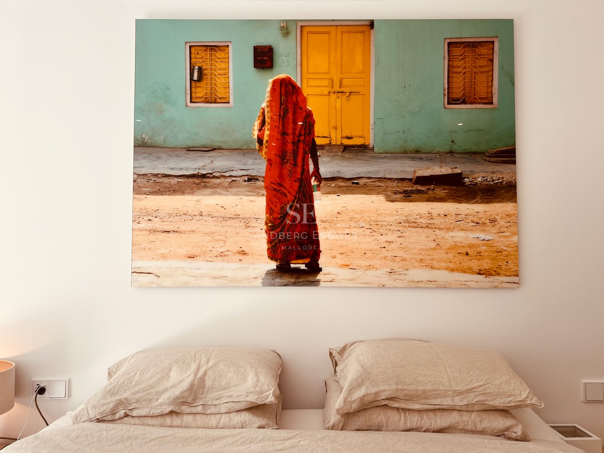 Large colorful artwork hanging above a bed with neutral linen pillows against a white wall.