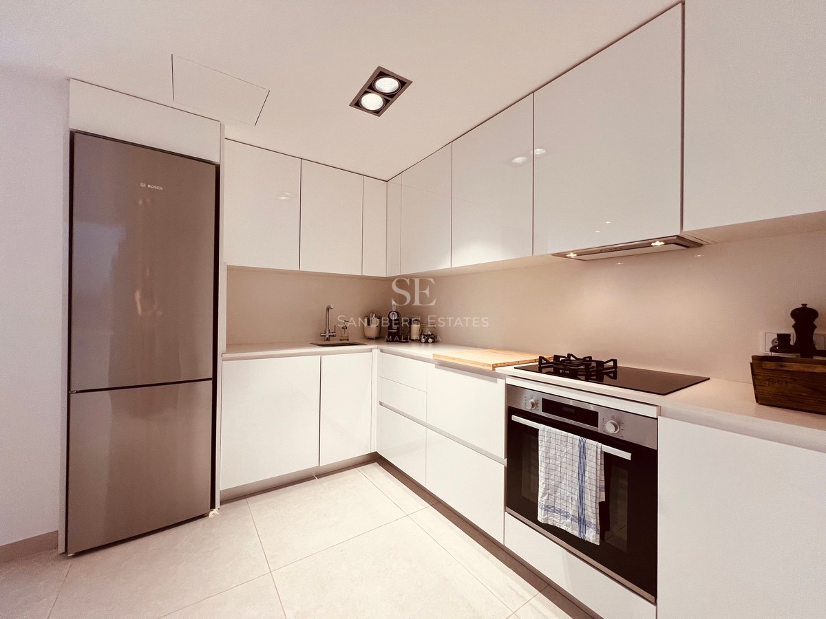 White high-gloss minimalist kitchen with built-in oven, glass cooktop, and recessed ceiling lighting.
