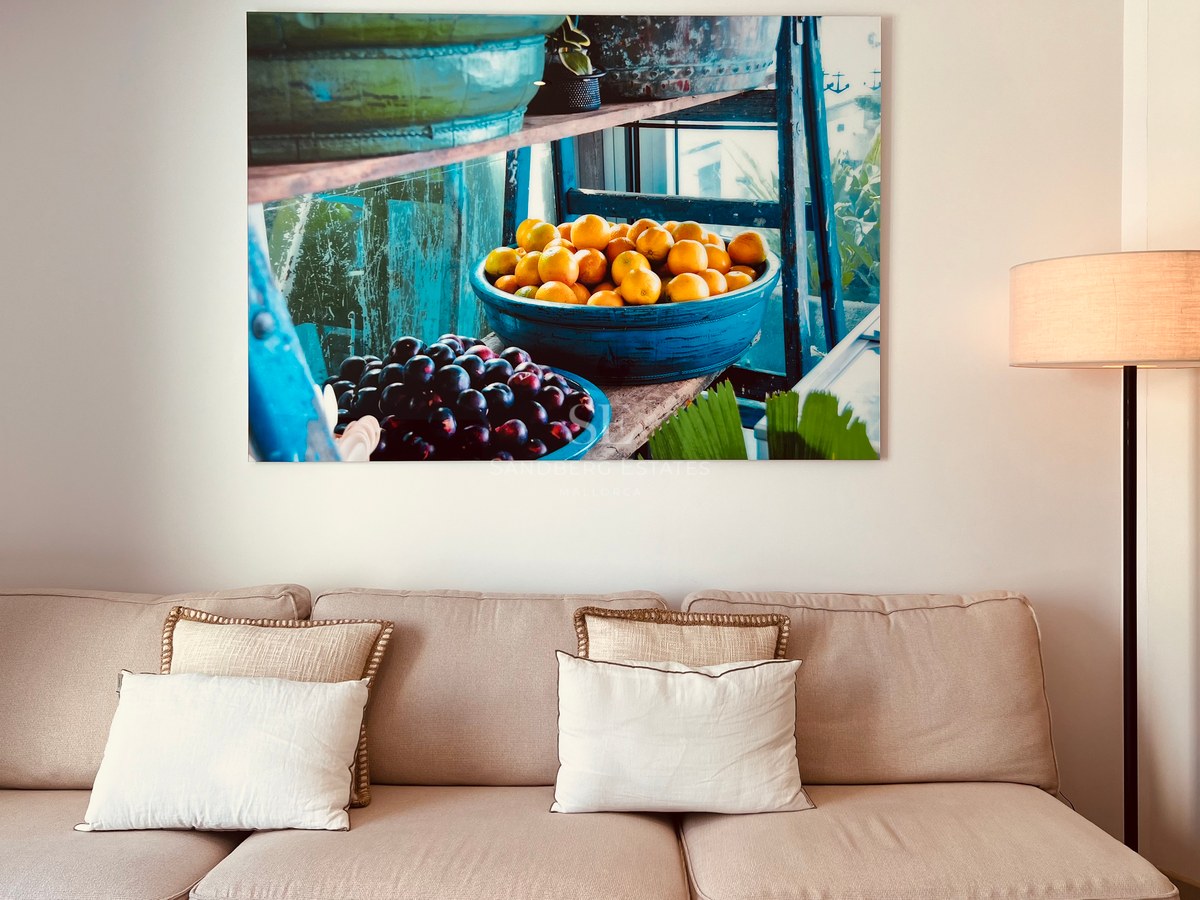 Beige sofa with decorative pillows below a large canvas painting of fruit in blue bowls.