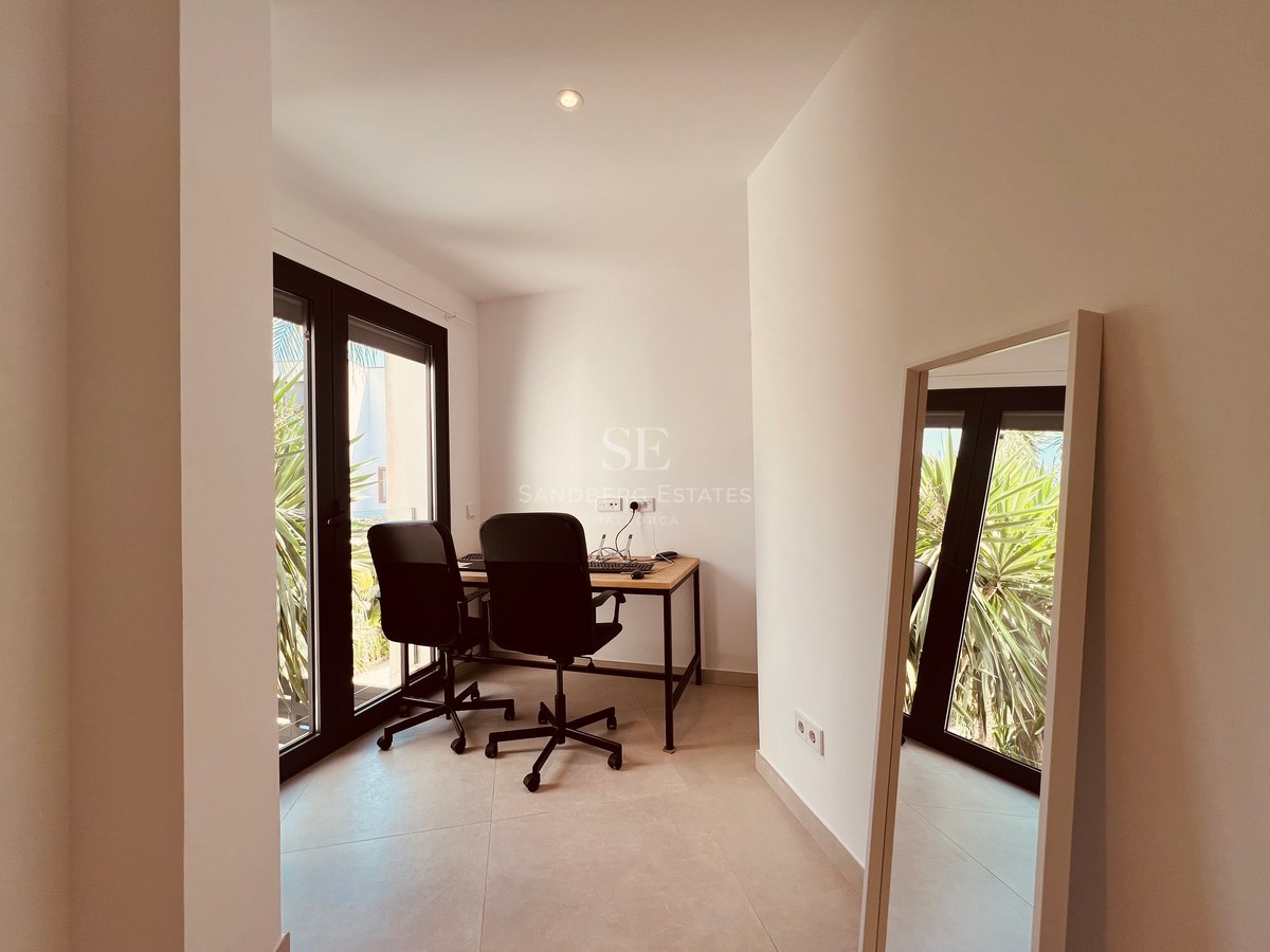 Bright contemporary home office featuring a wooden desk, two ergonomic chairs, and large glass doors to the garden.