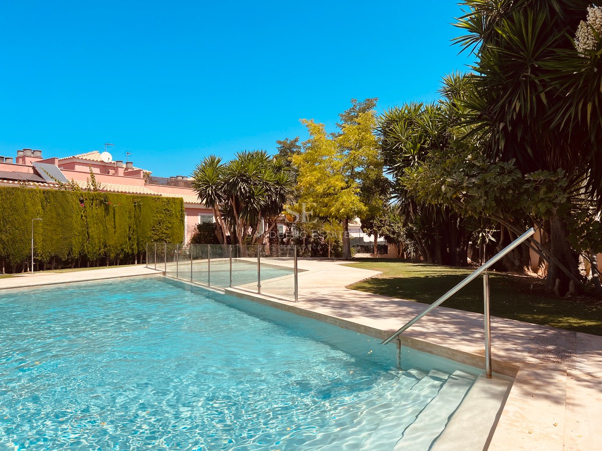 Close-up of a swimming pool with turquoise water, a stone deck, and glass fencing, framed by lush palm trees.