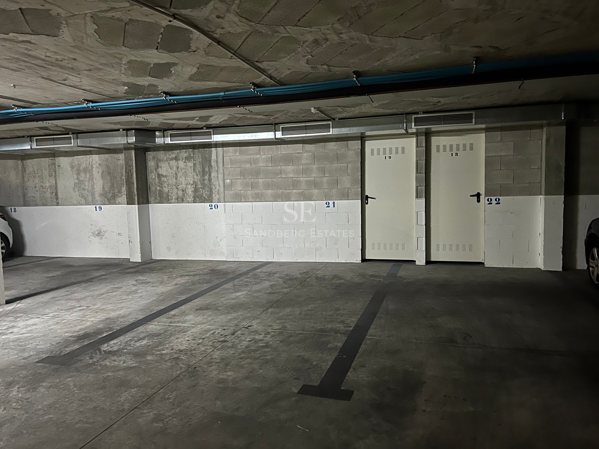 Underground parking garage with concrete floors, numbered spaces, and white metal storage room doors.