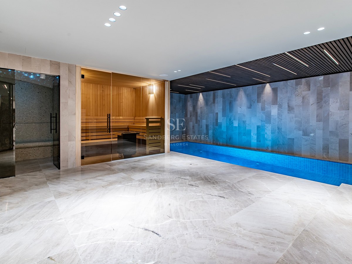 Modern indoor spa area featuring a marble floor, a glass-fronted sauna, and a long blue lap pool under accent lighting.