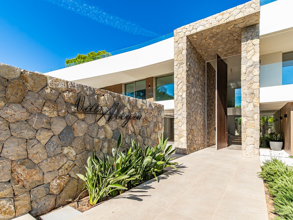 Modern villa entrance featuring a dry stone wall with Villa Alegra signage and a large wood pivot door.