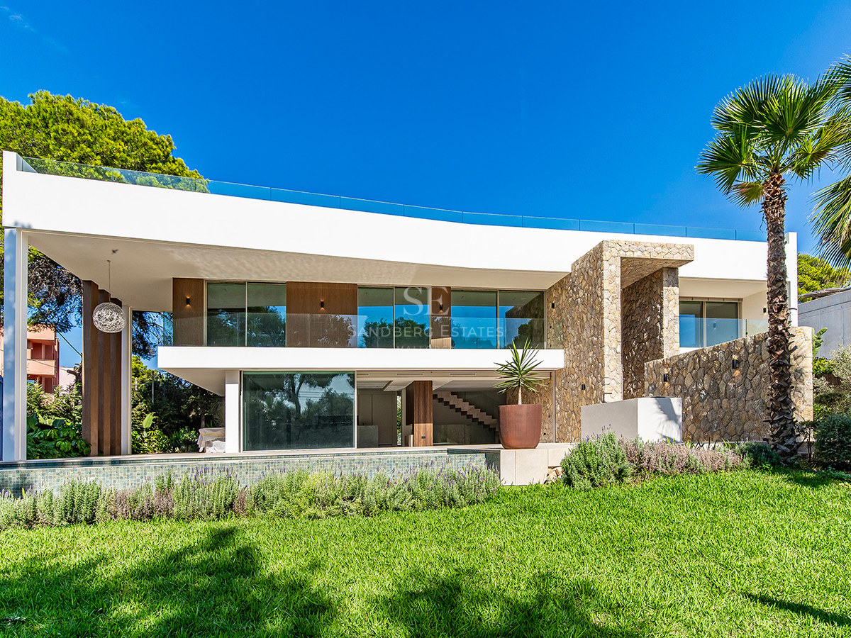 Exterior of a white two-story modern villa with stone walls, glass balconies, pool, and manicured green lawn.