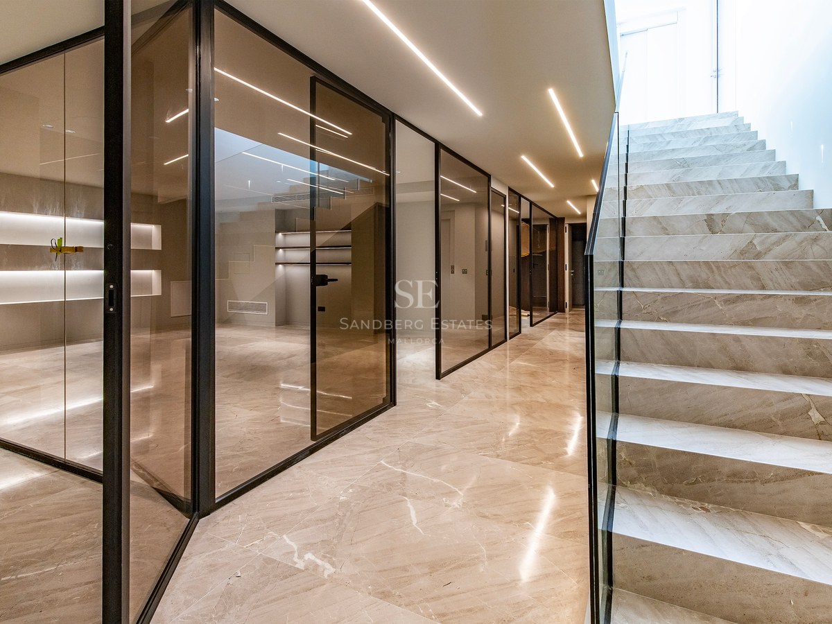 Modern interior hallway featuring a marble staircase, floor-to-ceiling glass partitions, and linear LED ceiling lighting.