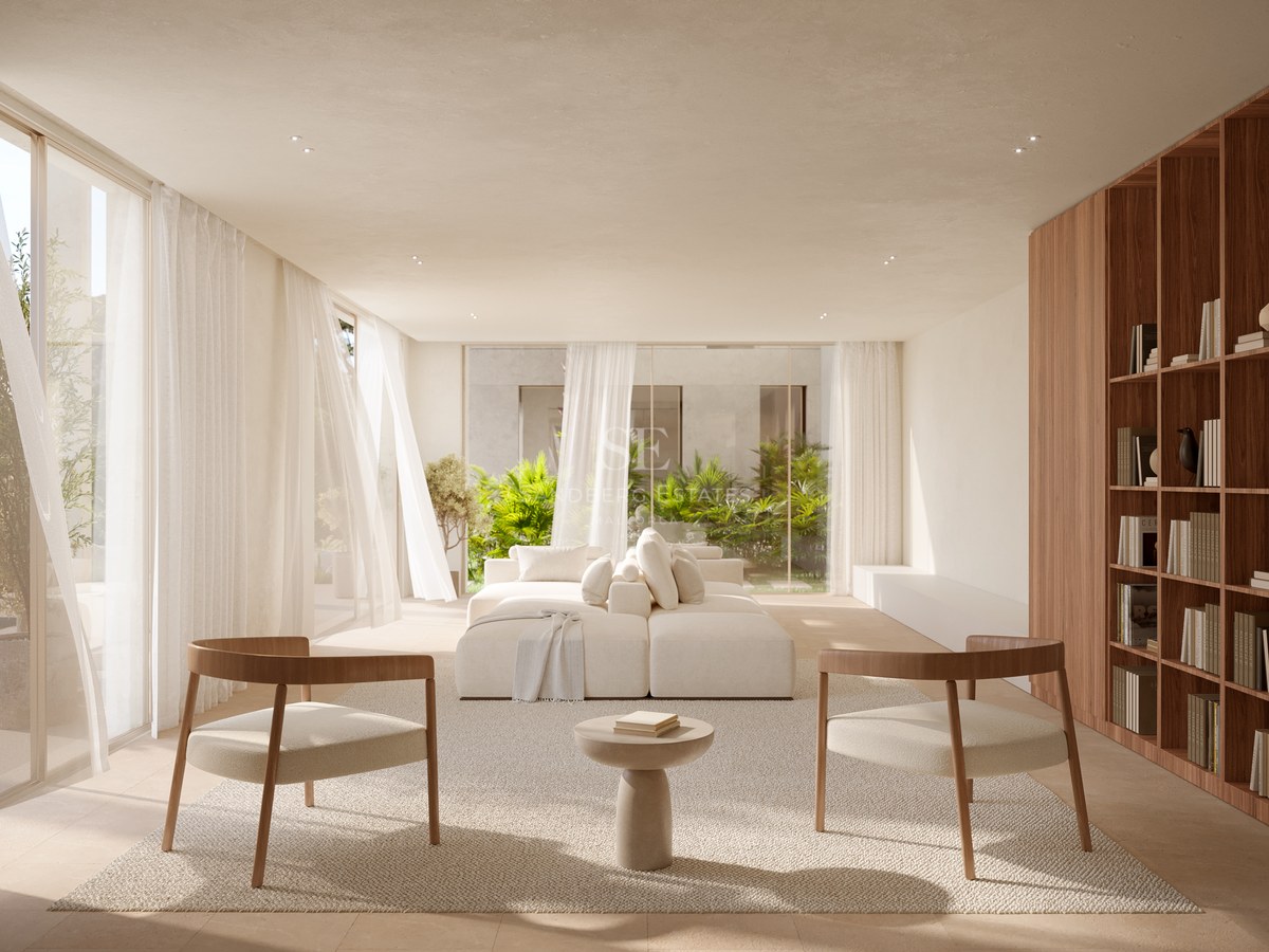 Bright living room with white modular sofa, two wooden armchairs, and floor-to-ceiling windows overlooking a garden.