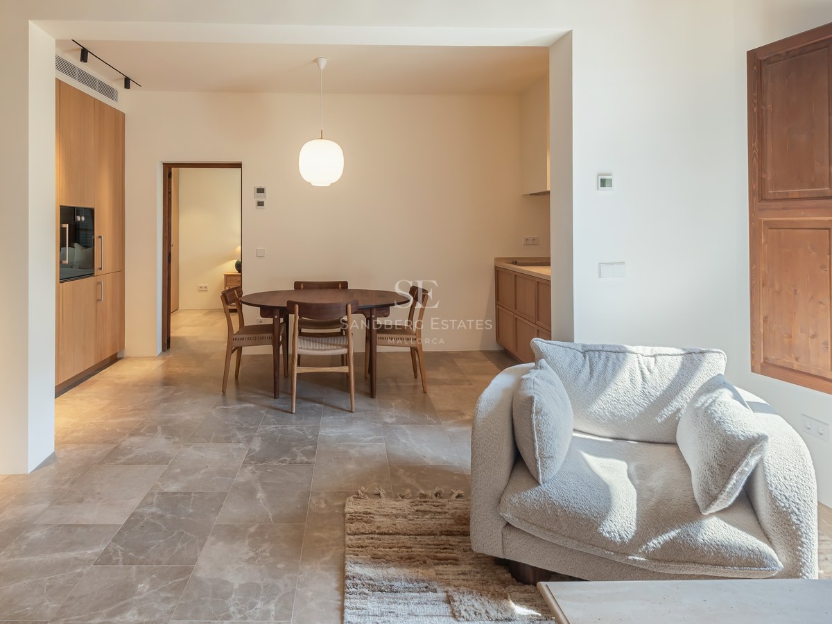 Salon moderne avec sol en pierre, menuiserie en bois, table ronde et fauteuil en bouclé blanc près d'une fenêtre.