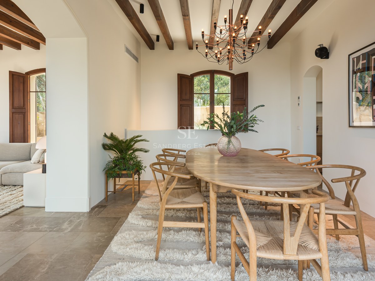 Salle à manger avec table ovale en bois, chaises style Wishbone, tapis en laine et plafond à poutres apparentes.
