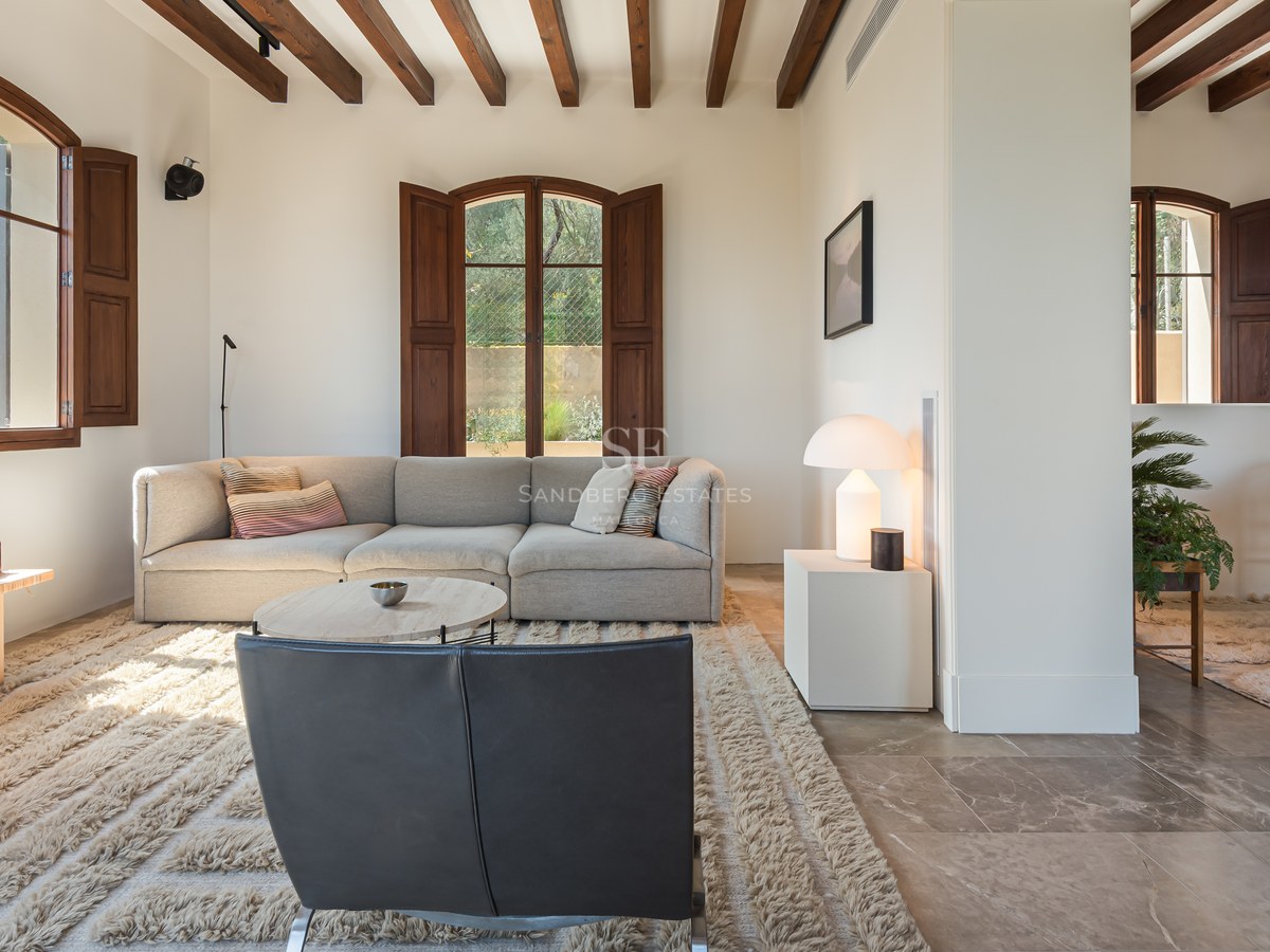Salon contemporain avec poutres en bois foncé, sol en pierre naturelle et mobilier design aux tons neutres.