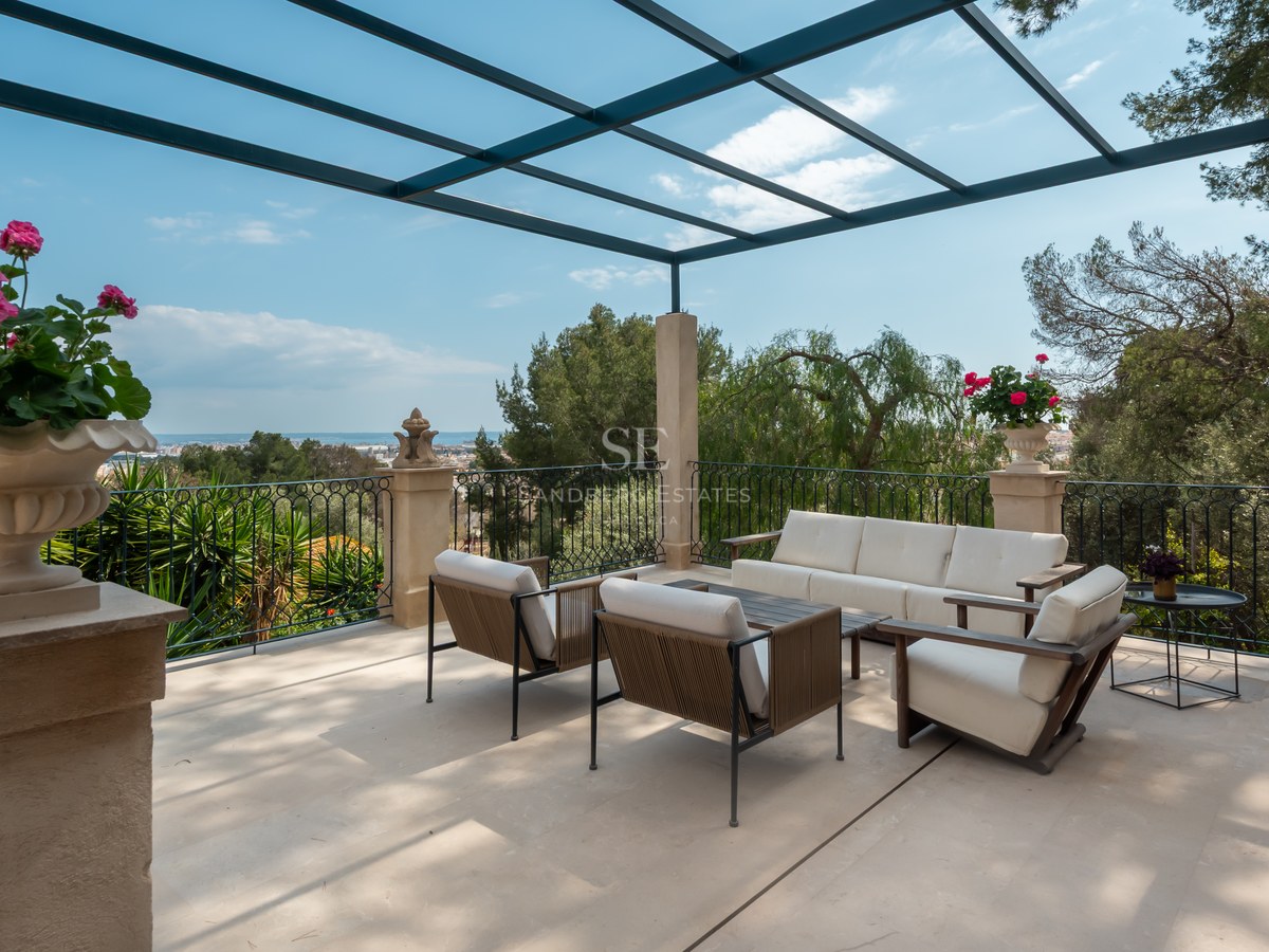 Terrasse ensoleillée avec mobilier lounge moderne, garde-corps en fer forgé et pergola métallique surplombant la côte.