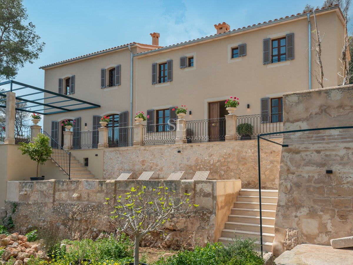 Élégante villa méditerranéenne beige de deux étages avec volets gris-bleu, murs de terrasse en pierre et garde-corps.