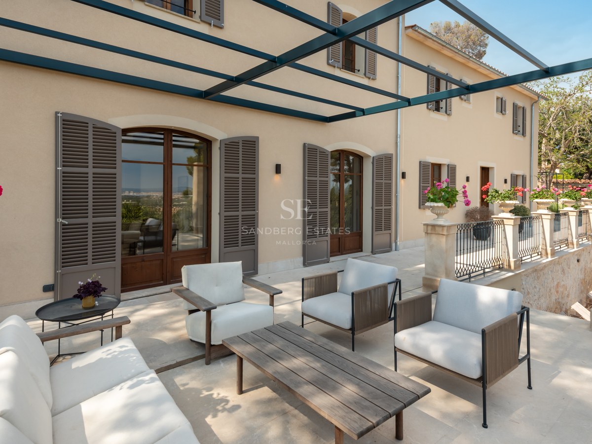 Terrasse de villa de luxe avec mobilier moderne, pergola en métal et volets majorquins traditionnels.