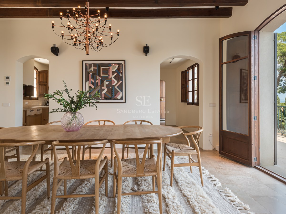 Table à manger ovale en chêne, chaises wishbone et poutres apparentes dans une luxueuse résidence méditerranéenne.