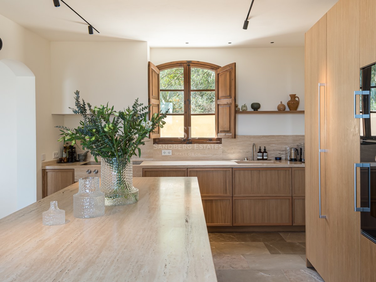 Cuisine minimaliste avec placards en chêne clair, îlot en travertin et volets en bois traditionnels.