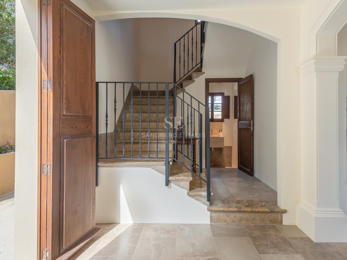 Entrée avec escalier en pierre, rampe en fer forgé, sols en marbre et porte en bois dans une villa de luxe.