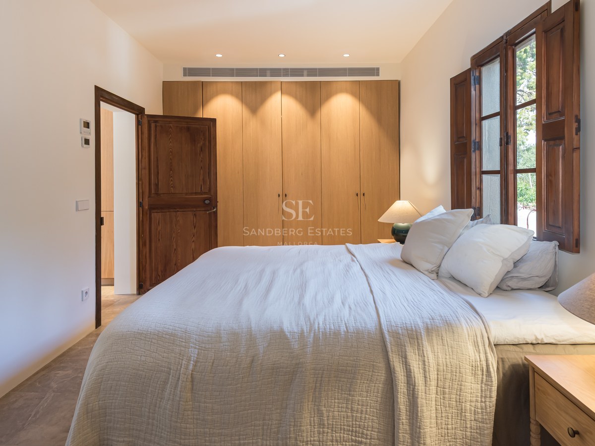 Chambre avec grand lit, placards intégrés en bois et volets majorquins sous une lumière chaleureuse.