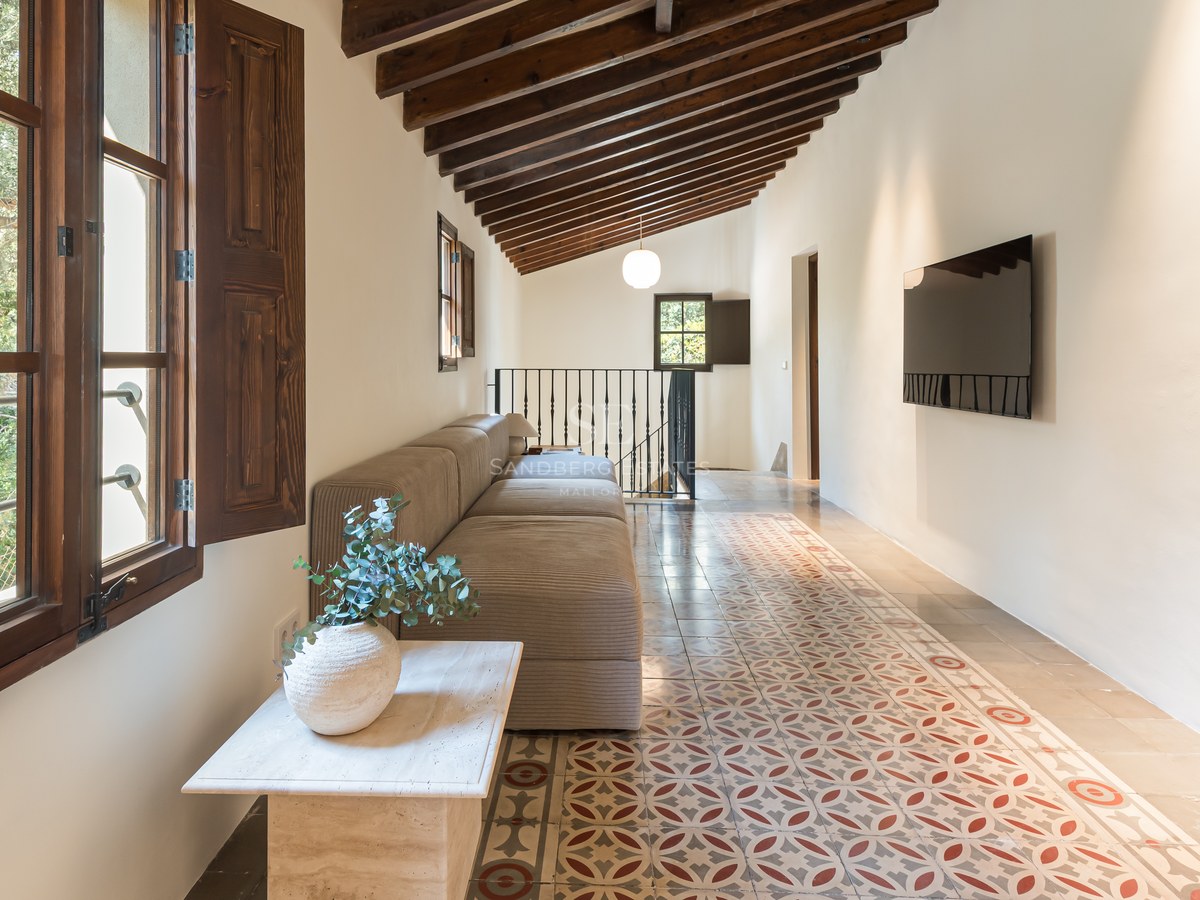 Espace de vie avec poutres apparentes, carreaux de ciment traditionnels, canapé modulaire et volets en bois.