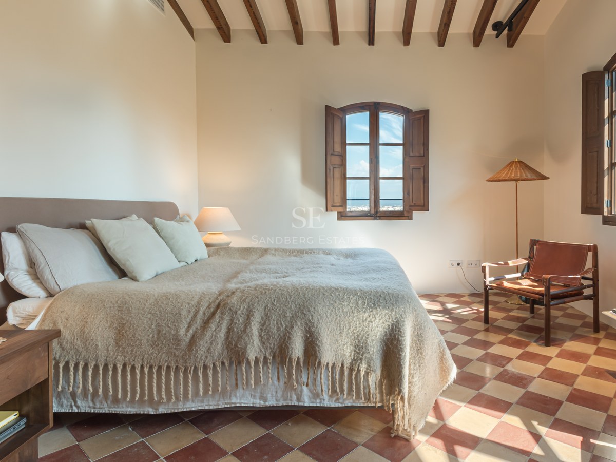 Chambre rustique avec sol en terre cuite, poutres apparentes et fenêtres à volets en bois donnant sur la côte.