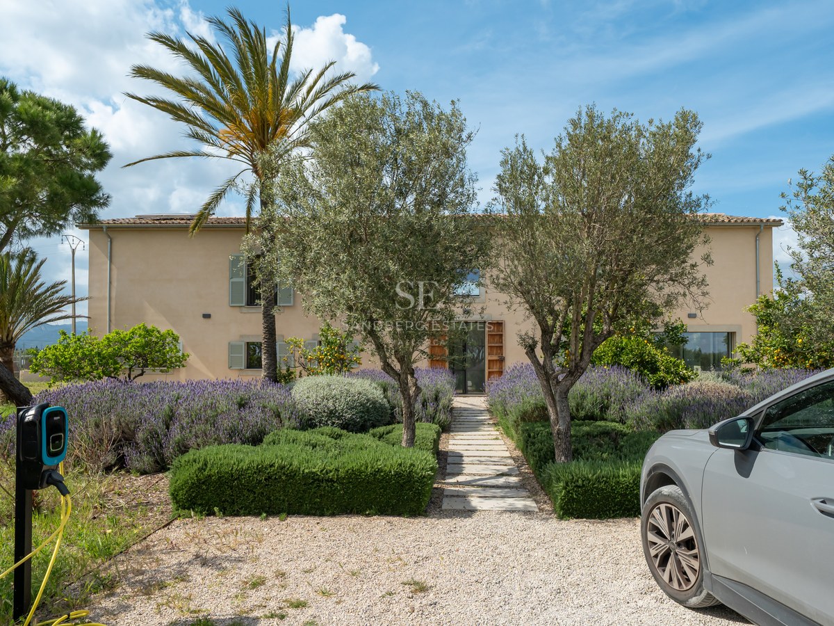 Fasad av sandfärgad villa med lavendelträdgård, stenstig och elbilsladdare på uppfarten.