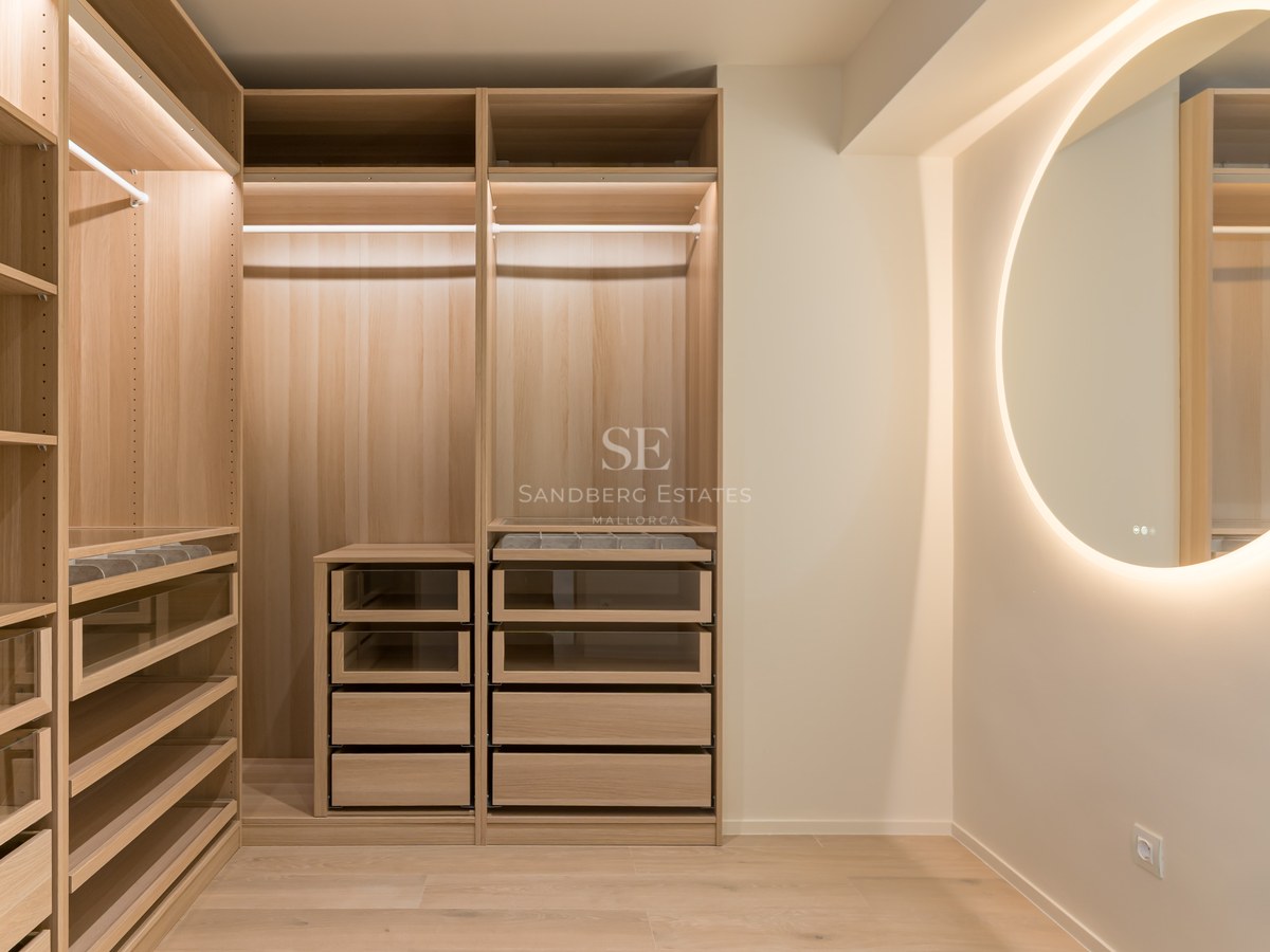 Vestidor moderno con armarios de roble claro, cajones con frente de cristal y un gran espejo circular retroiluminado.