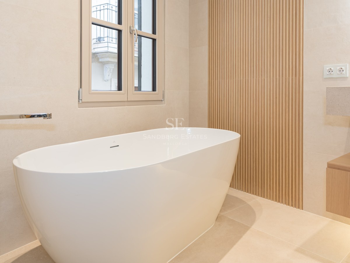 Bañera blanca exenta junto a pared de listones de madera y grifería cromada sobre suelo de piedra natural.